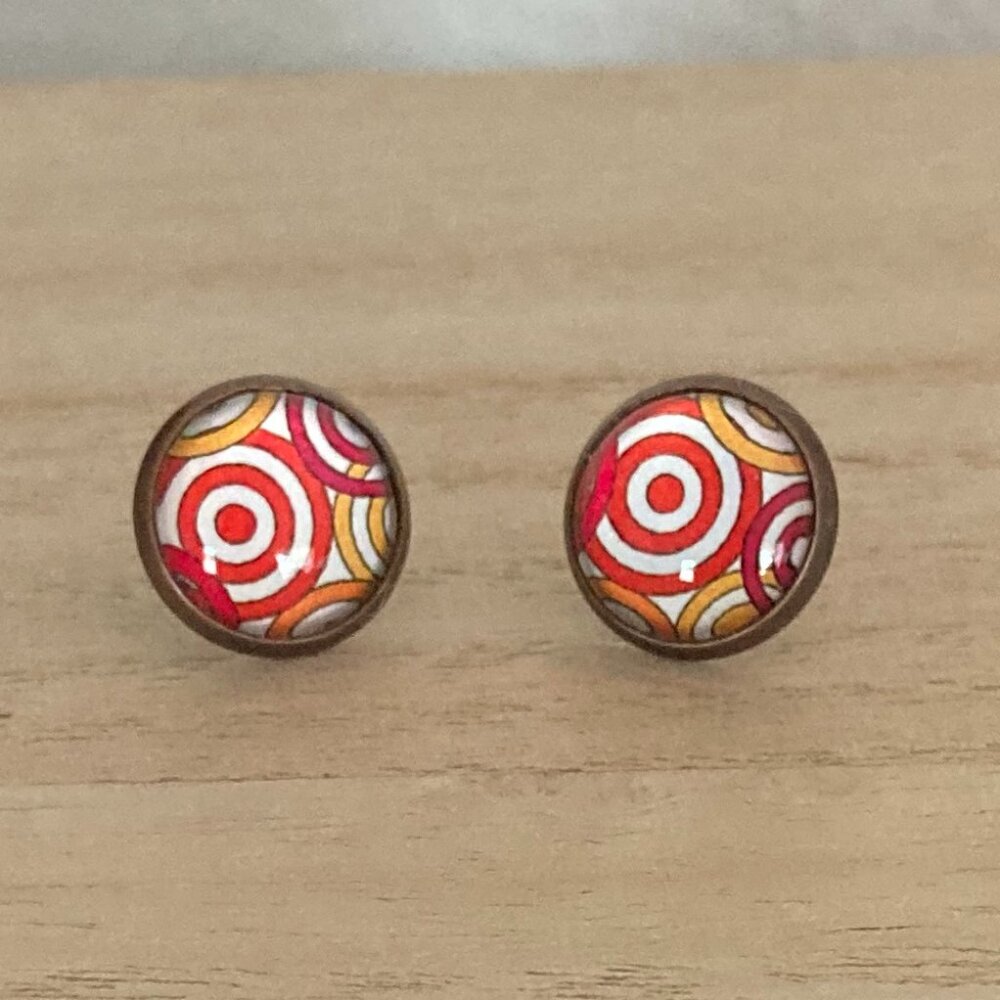 Stud earrings. Glass dome over a red, yellow and white pattern.